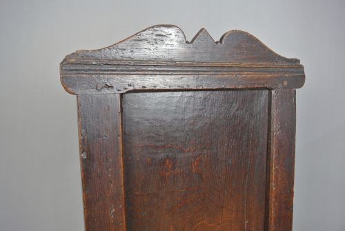 fig 2. A 17th-century Jacobean dark oak wainscot armchair featuring a high panelled back, straight arms, and heavy square legs joined by stretchers.