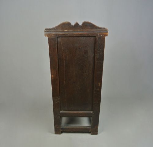 fig 3. A 17th-century Jacobean dark oak wainscot armchair featuring a high panelled back, straight arms, and heavy square legs joined by stretchers.