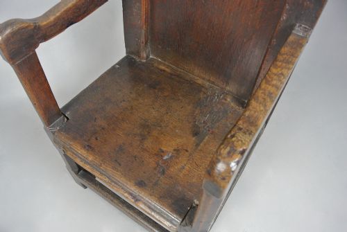 fig 4. A 17th-century Jacobean dark oak wainscot armchair featuring a high panelled back, straight arms, and heavy square legs joined by stretchers.