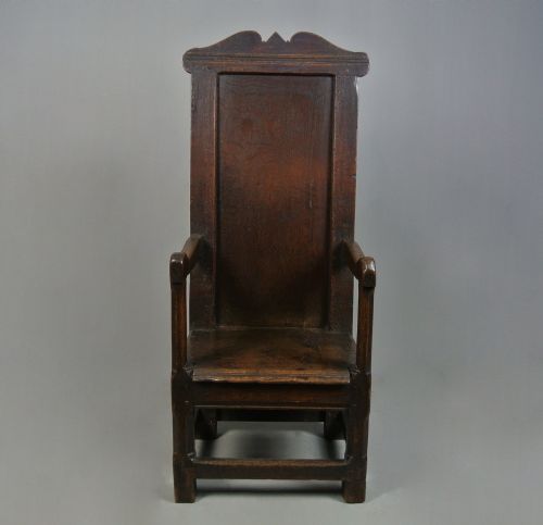 fig 5. A 17th-century Jacobean dark oak wainscot armchair featuring a high panelled back, straight arms, and heavy square legs joined by stretchers.
