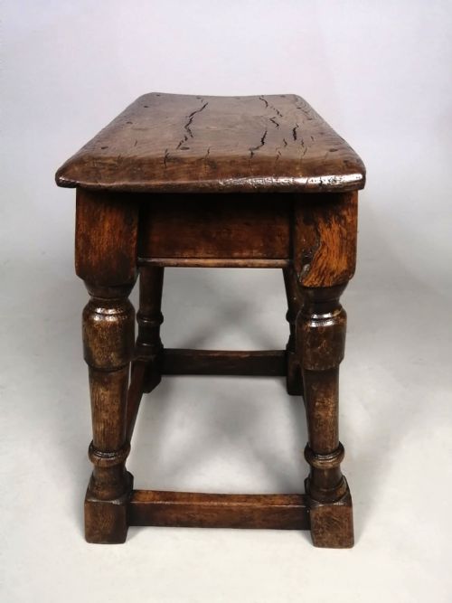 fig 1. An antique dark oak and elm joint stool featuring turned legs, peg joinery, a square stretcher base, and a rectangular timber seat.
