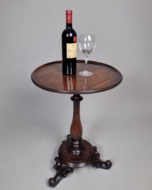 fig 2. A William IV mahogany wine table featuring a dished circular top, turned central pedestal column, and a carved triform base with scroll feet.