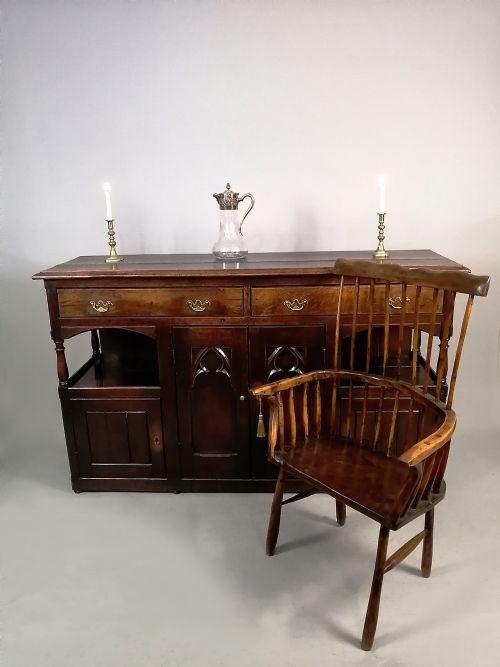 fig 4. A George III dark oak low dresser featuring central cupboard doors with Gothic pointed arch panels, upper drawers with brass swan-neck handles, and turned supports.