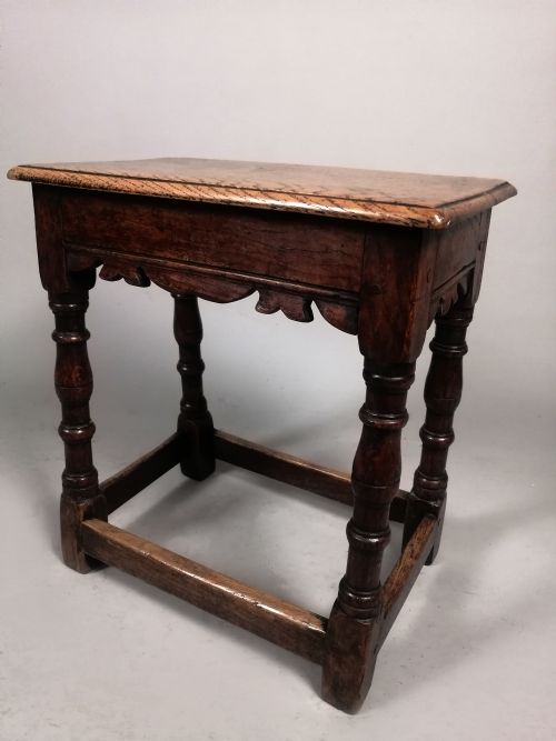 fig 1. An early eighteenth-century dark oak joint stool featuring turned legs, a shaped frieze, perimeter stretchers, and a flat rectangular top.