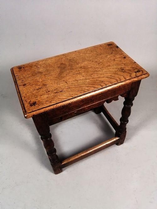 fig 2. An early eighteenth-century dark oak joint stool featuring turned legs, a shaped frieze, perimeter stretchers, and a flat rectangular top.