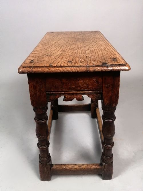fig 3. An early eighteenth-century dark oak joint stool featuring turned legs, a shaped frieze, perimeter stretchers, and a flat rectangular top.