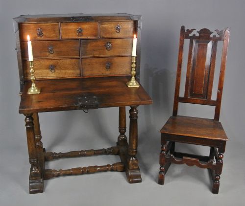 fig 1. A 17th-century dark oak strong box featuring a fall-front desk opening to reveal small internal drawers, resting on a turned stand with stretchers.