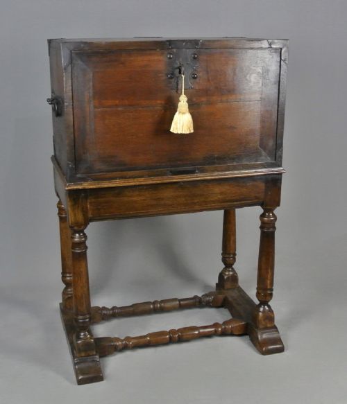 fig 2. A 17th-century dark oak strong box featuring a fall-front desk opening to reveal small internal drawers, resting on a turned stand with stretchers.