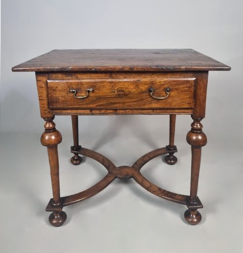 fig 2. A Queen Anne period oak and elm lowboy featuring a single drawer with brass drop handles, turned legs, and a curved X-frame stretcher.