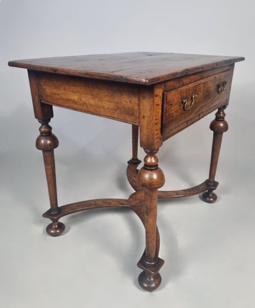 fig 4. A Queen Anne period oak and elm lowboy featuring a single drawer with brass drop handles, turned legs, and a curved X-frame stretcher.