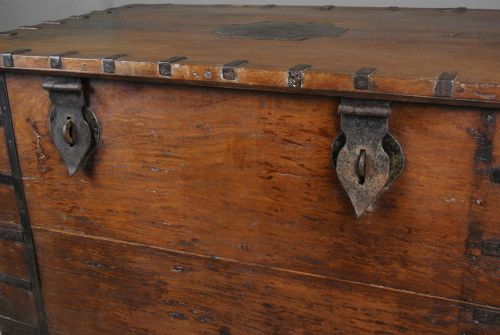 fig 2. A large brown teak wood chest reinforced with dark iron straps, corner brackets, side handles, and front latches.