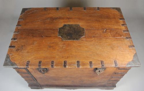 fig 3. A large brown teak wood chest reinforced with dark iron straps, corner brackets, side handles, and front latches.