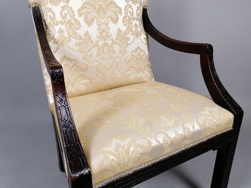 fig 3. A George II mahogany library chair upholstered in cream damask fabric featuring carved Chinese Chippendale fretwork on the legs and arms.