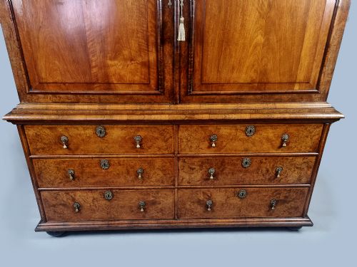 fig 3. A Queen Anne burr walnut press cupboard featuring a double-door upper section above six lower drawers with brass drop handles.