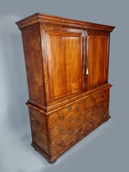 fig 4. A Queen Anne burr walnut press cupboard featuring a double-door upper section above six lower drawers with brass drop handles.