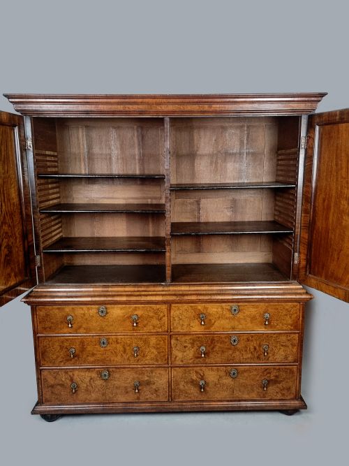 fig 5. A Queen Anne burr walnut press cupboard featuring a double-door upper section above six lower drawers with brass drop handles.