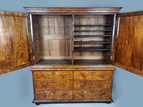 fig 6. A Queen Anne burr walnut press cupboard featuring a double-door upper section above six lower drawers with brass drop handles.