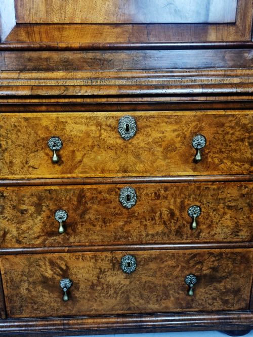 fig 8. A Queen Anne burr walnut press cupboard featuring a double-door upper section above six lower drawers with brass drop handles.