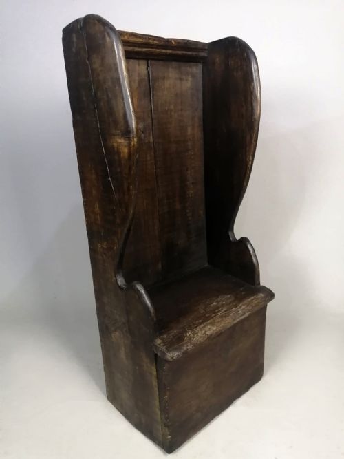 fig 2. A dark fruitwood childs lambing chair featuring a tall panelled back, enclosed wing sides, and a solid rectangular box base.