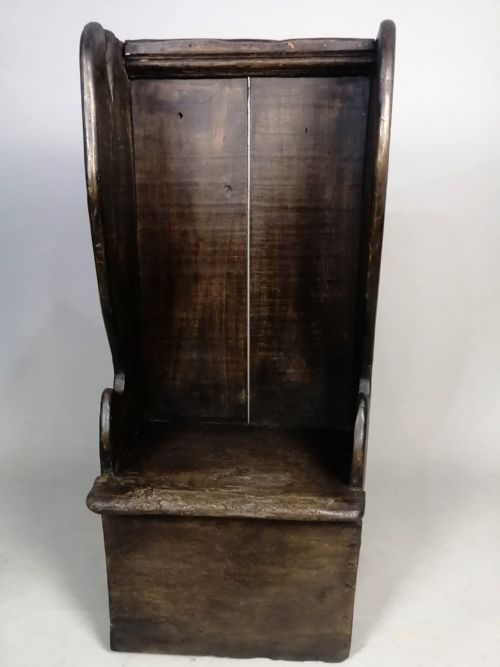 fig 3. A dark fruitwood childs lambing chair featuring a tall panelled back, enclosed wing sides, and a solid rectangular box base.