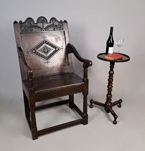 fig 1. A dark oak wainscot armchair featuring a carved lozenge motif on the back panel, shaped cresting rail, shaped armrests, and turned front legs with lower stretchers.