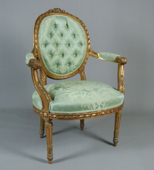 fig 1. An 18th-century George III giltwood armchair featuring a button-tufted oval back rest upholstered in light green damask fabric with carved gold leaf detail.
