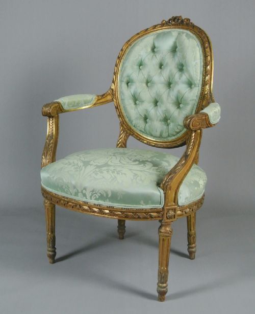 fig 2. An 18th-century George III giltwood armchair featuring a button-tufted oval back rest upholstered in light green damask fabric with carved gold leaf detail.