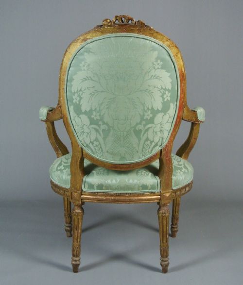 fig 3. An 18th-century George III giltwood armchair featuring a button-tufted oval back rest upholstered in light green damask fabric with carved gold leaf detail.