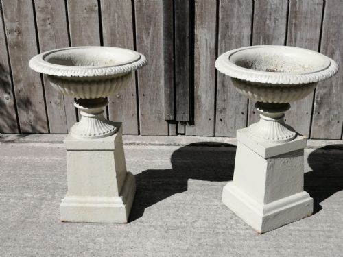 fig 1. A matching pair of painted off-white cast iron garden urns with fluted rims resting on square pedestals.