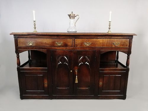fig 1. A dark oak George III dresser featuring four drawers above central Gothic arch cupboard doors, flanked by open shelves and lower side cupboards.
