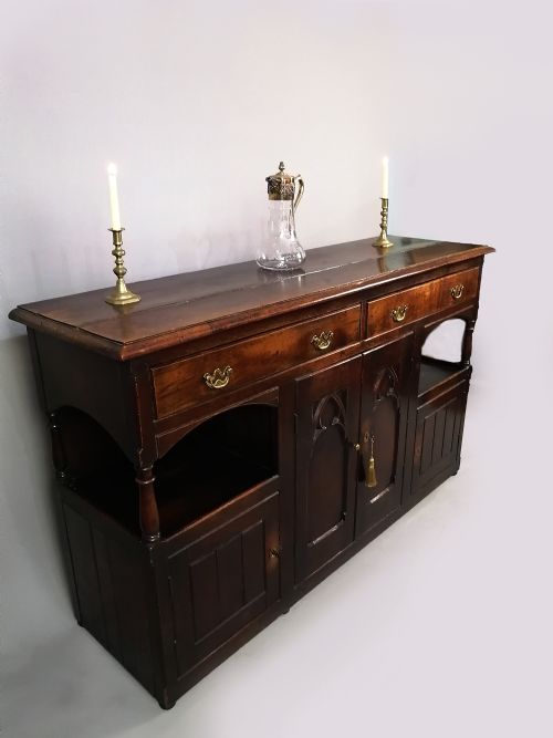 fig 2. A dark oak George III dresser featuring four drawers above central Gothic arch cupboard doors, flanked by open shelves and lower side cupboards.
