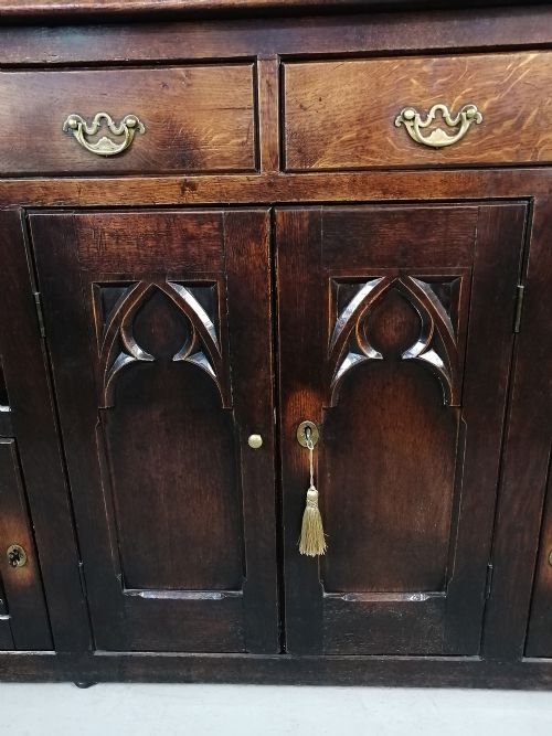 fig 5. A dark oak George III dresser featuring four drawers above central Gothic arch cupboard doors, flanked by open shelves and lower side cupboards.