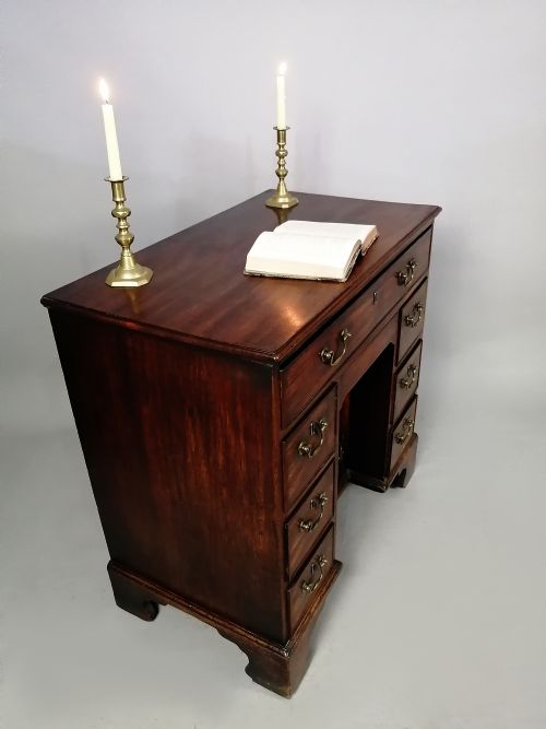 fig 2. A mid-18th century George II mahogany kneehole desk featuring a long top drawer over six side drawers and a central recessed cupboard on bracket feet.