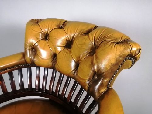 fig 1. A late Victorian revolving desk chair featuring mustard tan buttoned leather upholstery, brass studding, a mahogany spindle-back frame, and turned legs on castors.
