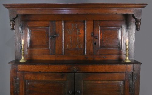 fig 1. An 18th-century dark oak court cupboard featuring a carved date of 1723, upper recessed cabinet with drop finials, and fielded lower door panels.