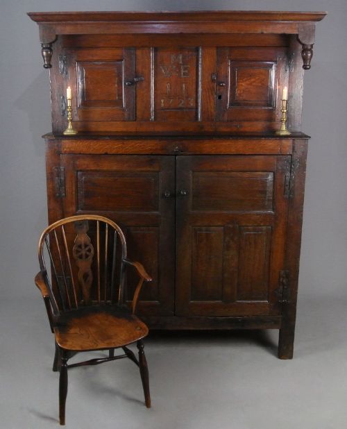 fig 2. An 18th-century dark oak court cupboard featuring a carved date of 1723, upper recessed cabinet with drop finials, and fielded lower door panels.