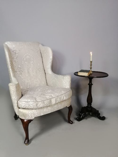 fig 1. A 19th-century English wingback armchair upholstered in cream damask fabric with dark carved walnut cabriole front legs.