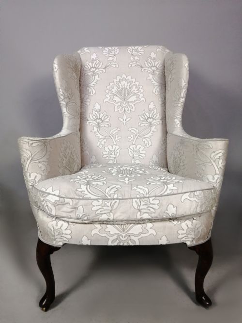 fig 2. A 19th-century English wingback armchair upholstered in cream damask fabric with dark carved walnut cabriole front legs.