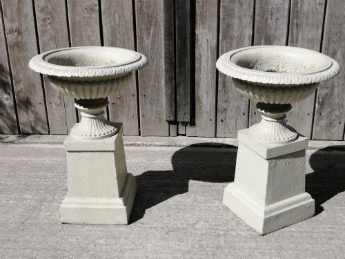 fig 1. A pair of off-white painted cast iron garden urns with fluted rims and bases set upon matching square plinth pedestals.