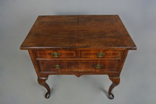 fig 2. A George I walnut lowboy table featuring three featherbanded drawers with brass handles, cabriole legs, pad feet, and a shaped apron.