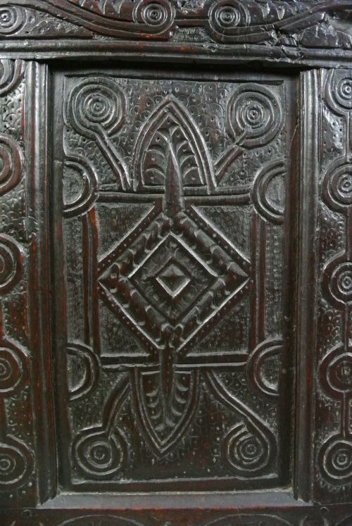 fig 2. A dark oak Jacobean coffer featuring three carved front panels with diamond and circle motifs, a lunette carved top rail, and stile legs.
