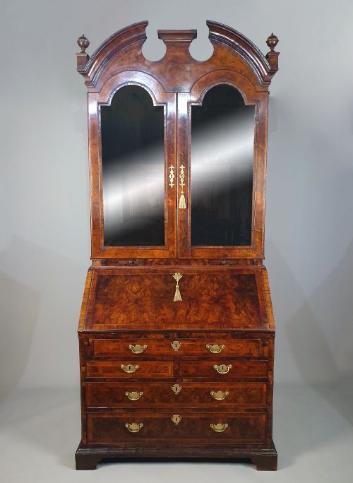 fig 2. An early 18th-century Queen Anne burr walnut bureau bookcase featuring an open double-domed upper cabinet with fitted interior pigeonholes above a fall-front desk section.