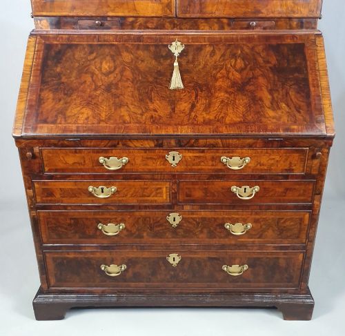 fig 3. An early 18th-century Queen Anne burr walnut bureau bookcase featuring an open double-domed upper cabinet with fitted interior pigeonholes above a fall-front desk section.