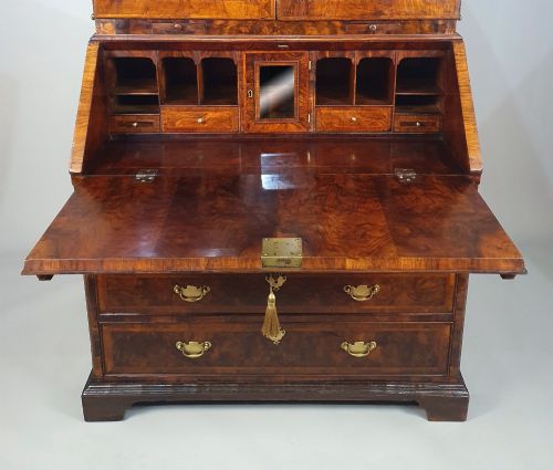 fig 4. An early 18th-century Queen Anne burr walnut bureau bookcase featuring an open double-domed upper cabinet with fitted interior pigeonholes above a fall-front desk section.
