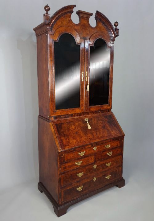 fig 7. An early 18th-century Queen Anne burr walnut bureau bookcase featuring an open double-domed upper cabinet with fitted interior pigeonholes above a fall-front desk section.