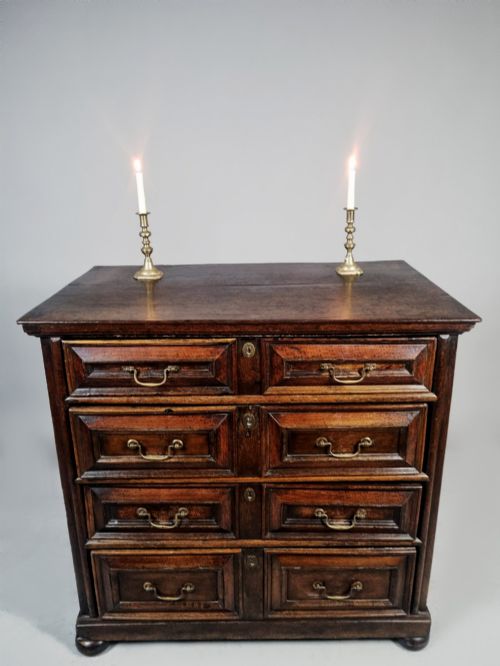 fig 2. A seventeenth-century dark oak chest of drawers featuring geometric mitred drawer panels, brass swing handles, and turned bun feet.