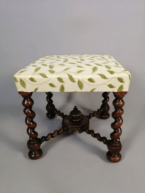 fig 2. A square dark walnut stool featuring spiral barley twist legs, a central finial stretcher, and cream upholstery with embroidered green leaf motifs.