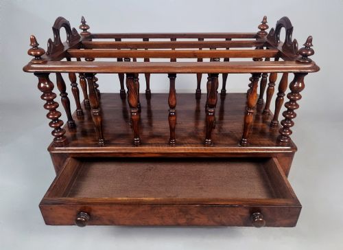 fig 4. A Victorian walnut Canterbury featuring vertical spindle dividers, a lower drawer base, carved side handles, and turned feet with brass castors.