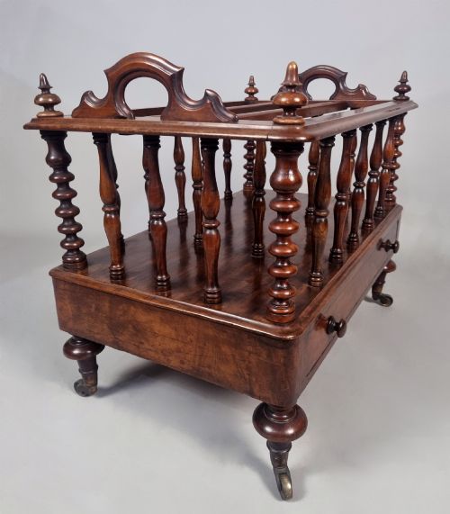 fig 5. A Victorian walnut Canterbury featuring vertical spindle dividers, a lower drawer base, carved side handles, and turned feet with brass castors.