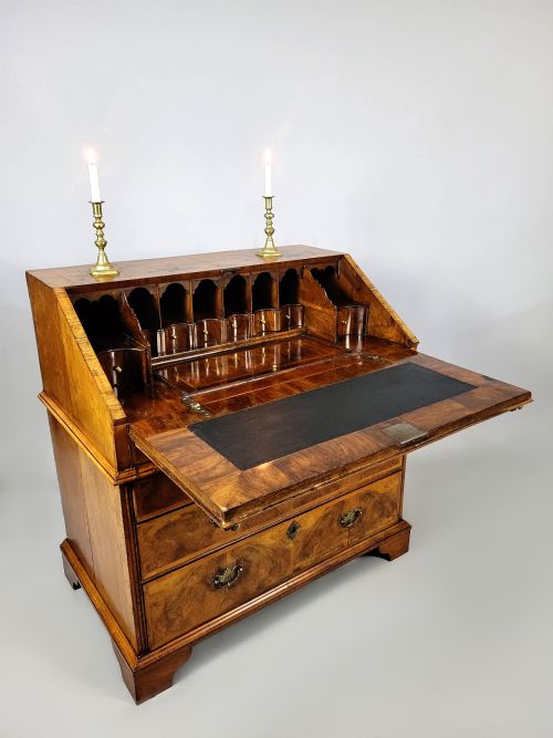 fig 3. An early 18th-century George I burr walnut bureau featuring a slant-front lid over graduating drawers with brass handles and bracket feet.